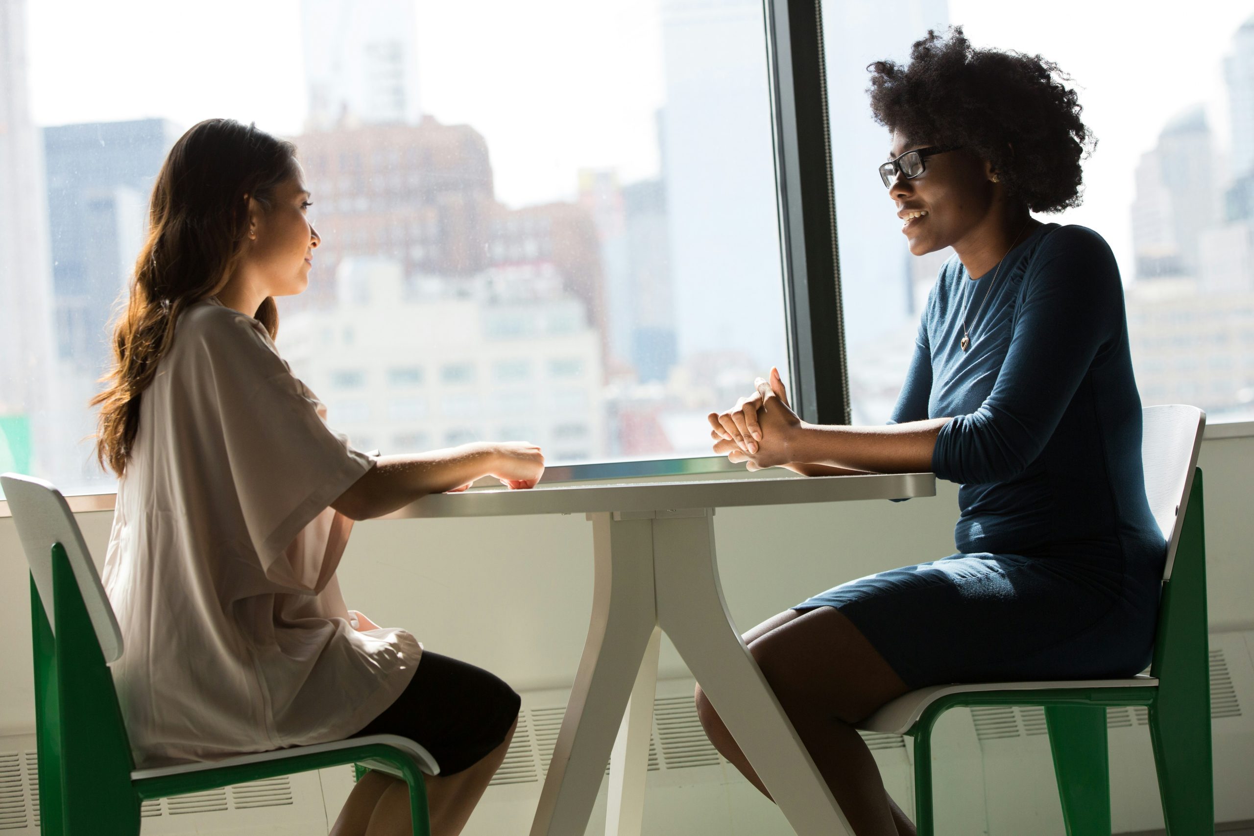Two women sitting beside a table and talking